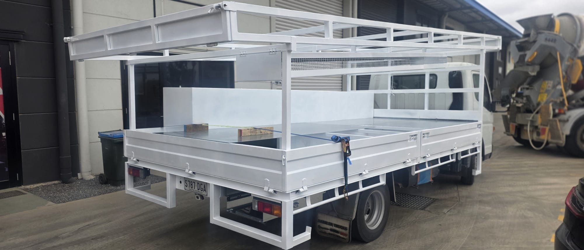 Freshly painted white custom tray body with overhead ladder rack fitted to a light truck.