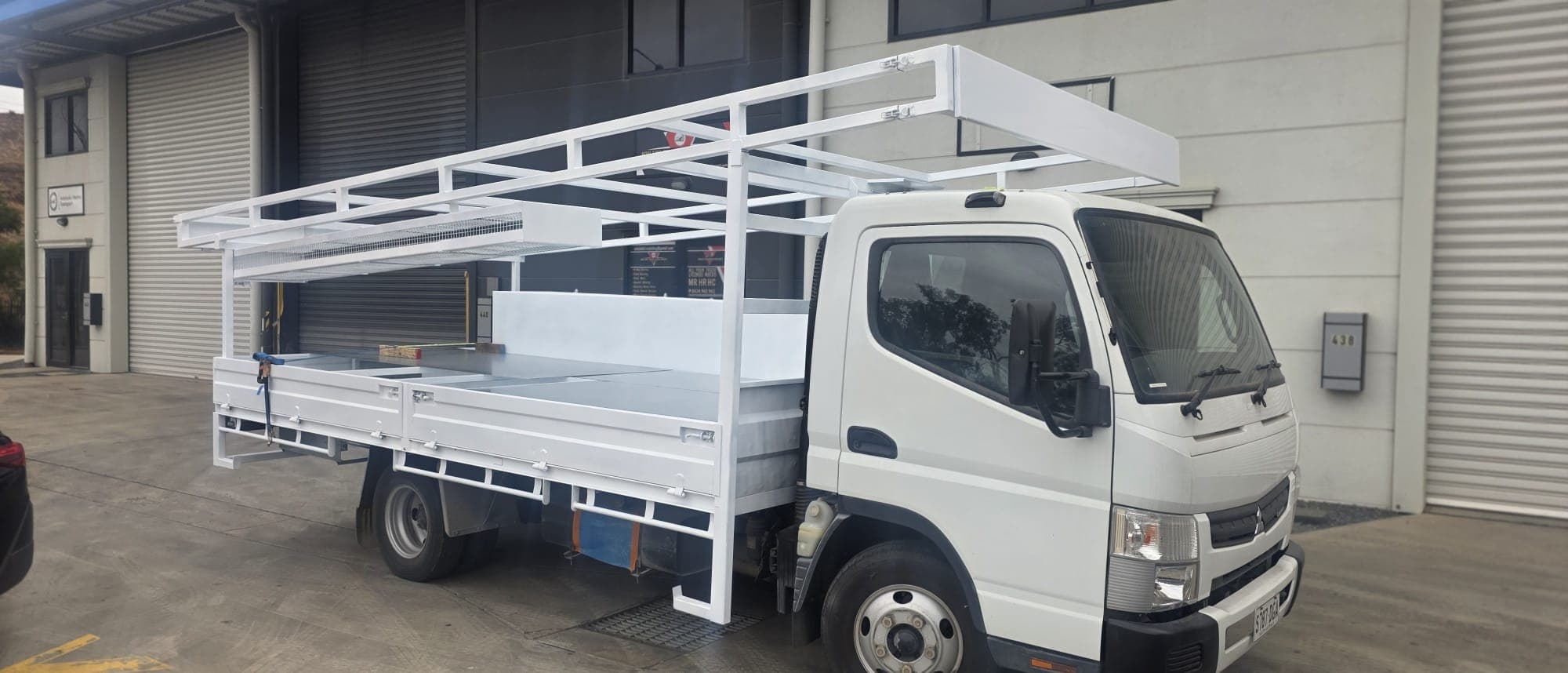 Fuso Canter fitted with a custom white steel tray and full-length ladder rack.