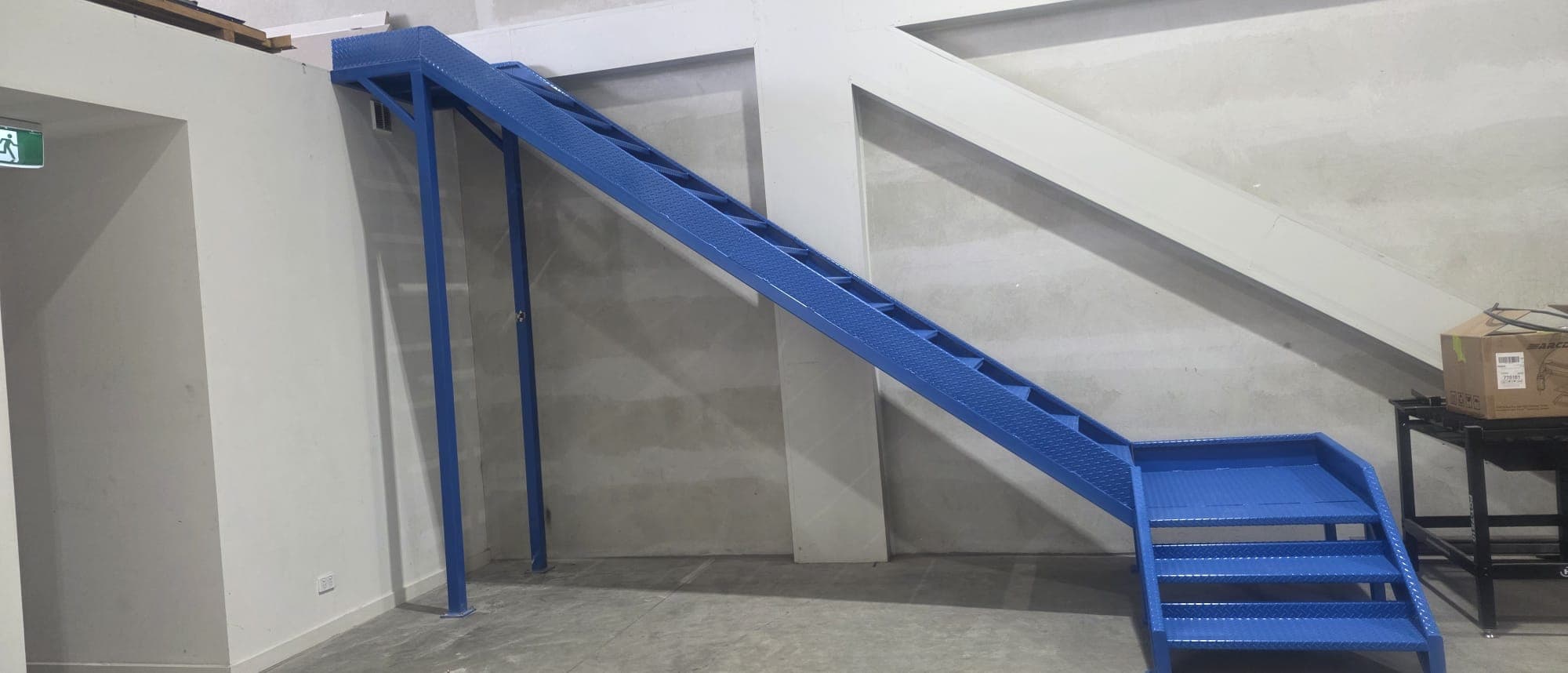 Blue steel mezzanine staircase with checker-plate treads installed on site.