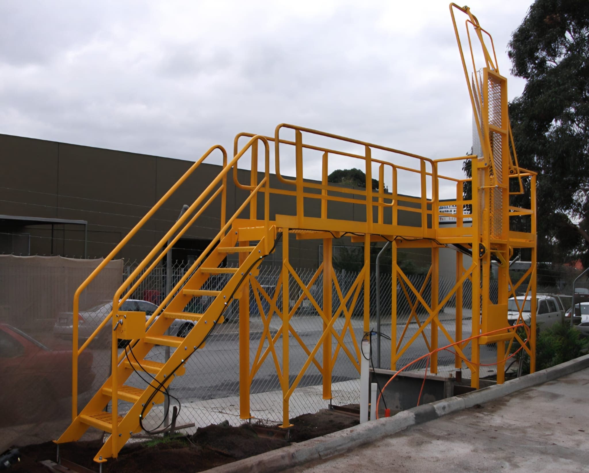 Safety-yellow steel access platform with stairs and handrails built by Kingpin Engineering.