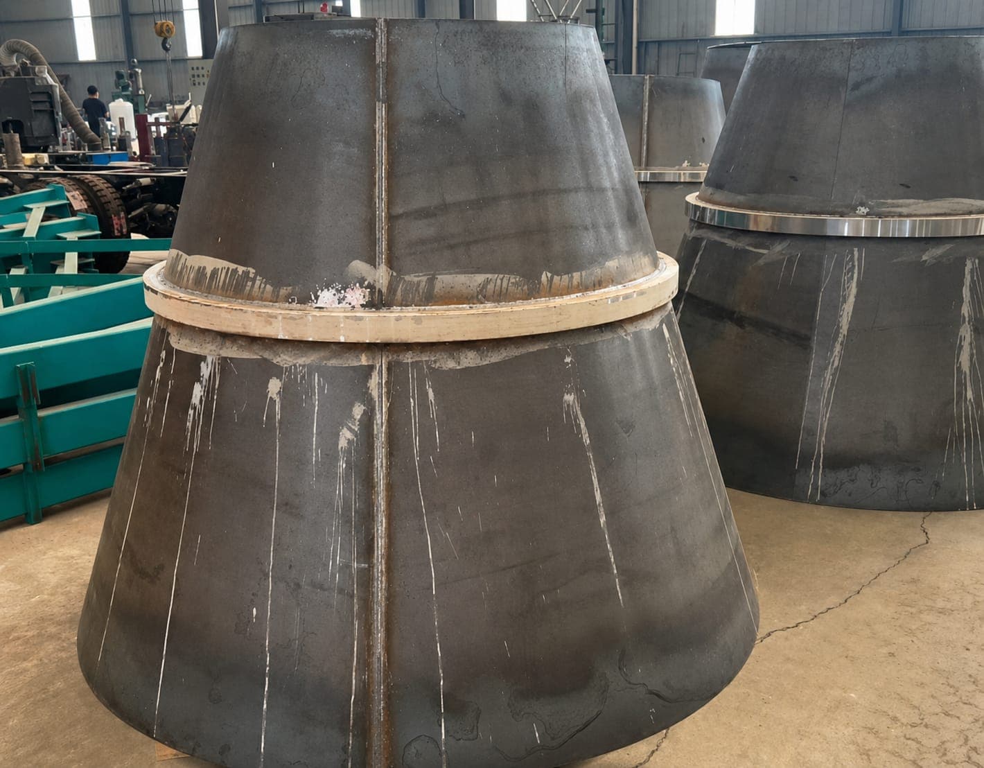 Rolled steel mixer drum cones lined up in the fabrication bay.